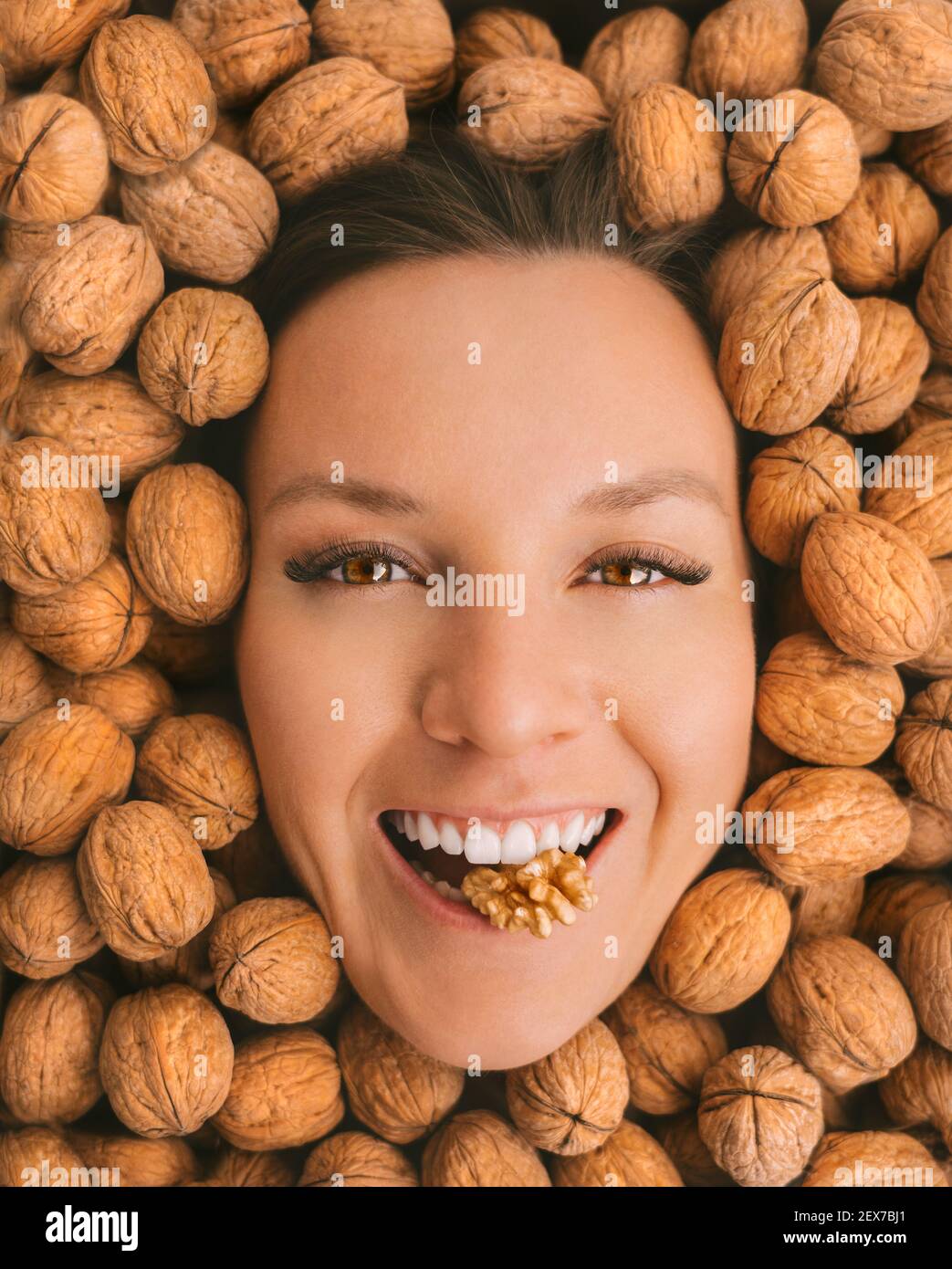 Happy smiling woman face on a walnuts background. Eating nuts. Healthy vegetarian protein and nutritious food. Woman with strong teeth and white smile Stock Photo