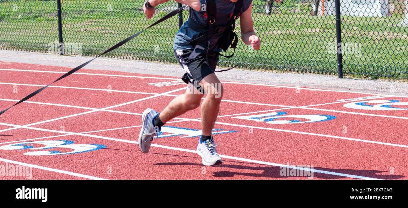 A high school track male track and field athlete is pulling a weighted