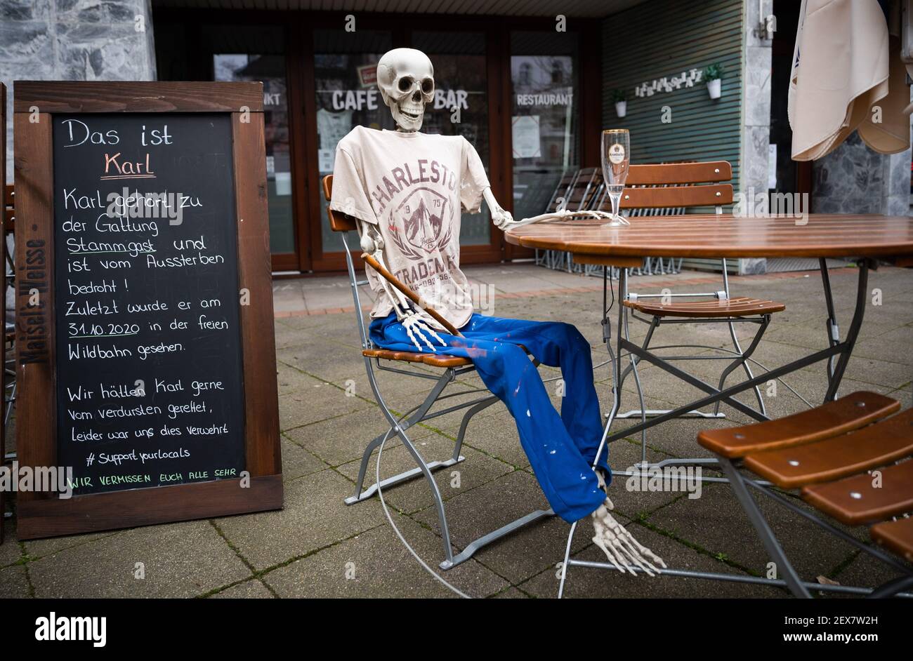 04 March 2021, Lower Saxony, Hanover: A skeleton sits with an empty beer glass outside a restaurant closed due to the Corona pandemic in Südstadt. The lockdown in Germany is extended until March 28. Photo: Julian Stratenschulte/dpa Stock Photo