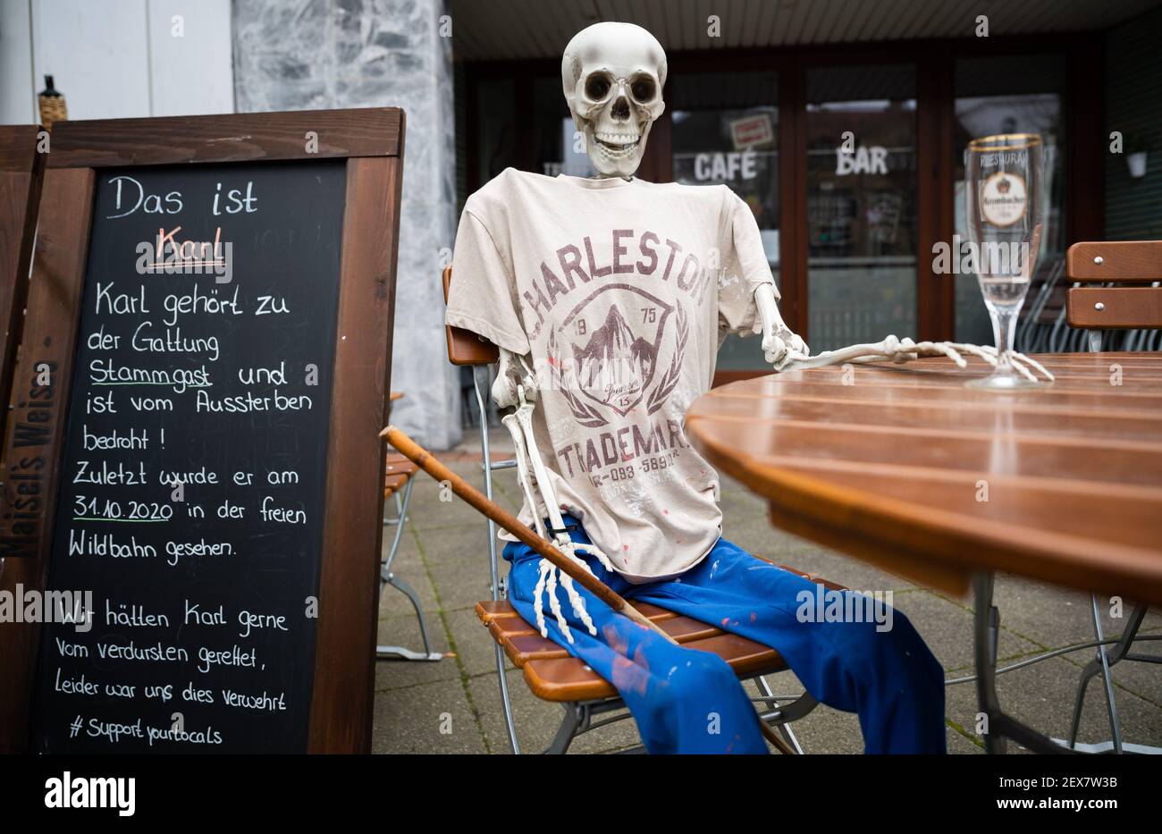 04 March 2021, Lower Saxony, Hanover: A skeleton sits with an empty beer glass outside a restaurant closed due to the Corona pandemic in Südstadt. The lockdown in Germany is extended until March 28. Photo: Julian Stratenschulte/dpa Stock Photo