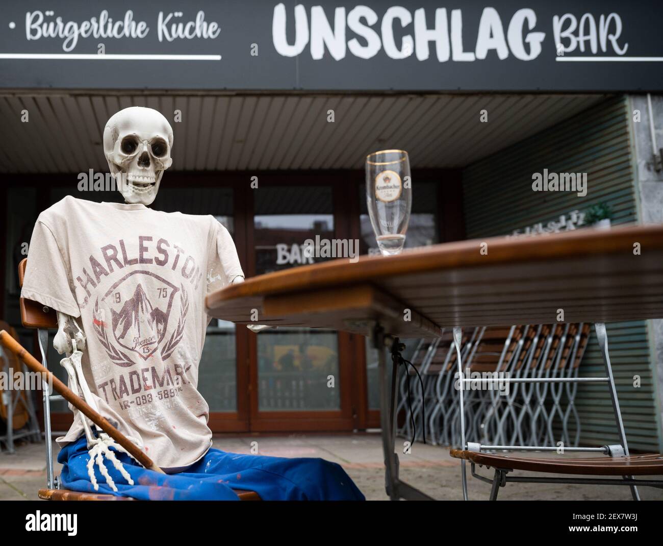 04 March 2021, Lower Saxony, Hanover: A skeleton sits with an empty beer glass outside a restaurant closed due to the Corona pandemic in Südstadt. The lockdown in Germany is extended until March 28. Photo: Julian Stratenschulte/dpa Stock Photo