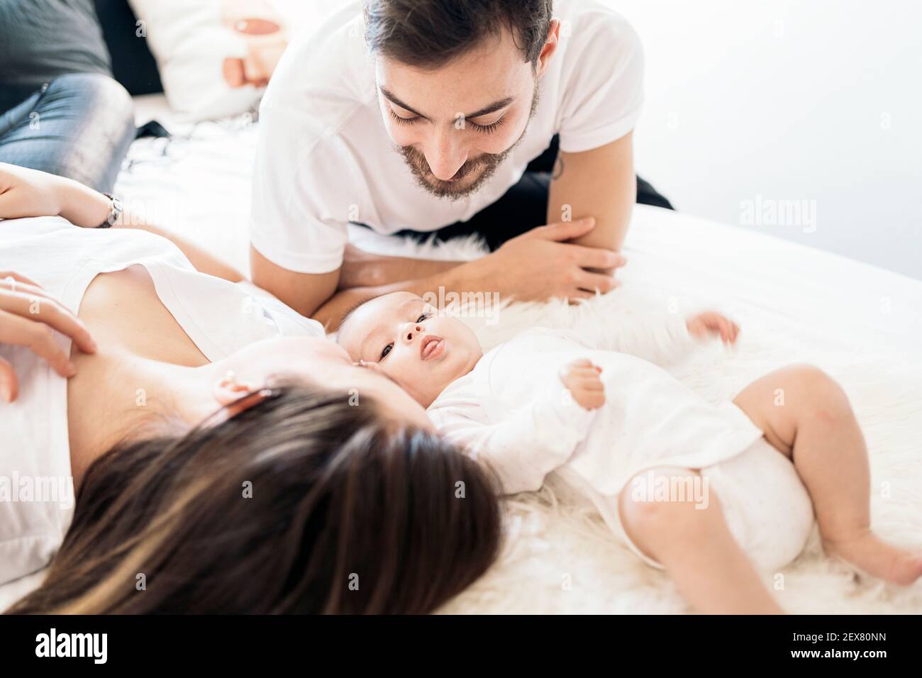 Stock photo of happy parents lying in bed with their adorable young baby. Stock Photo