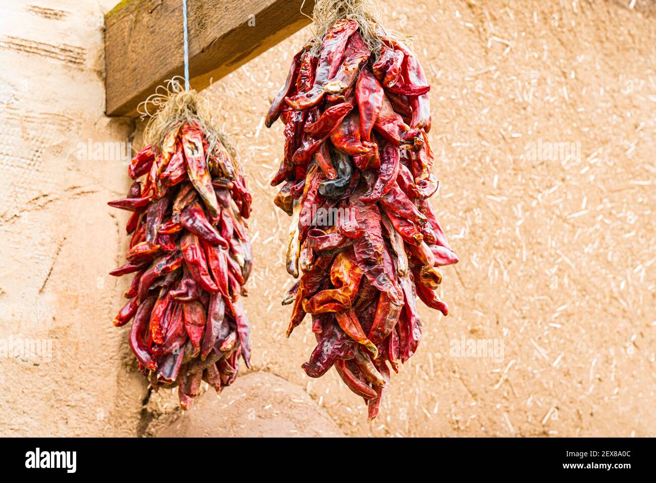 Two bunches of dried hot red chili peppers hanging outside of an adobe building in New Mexico Stock Photo