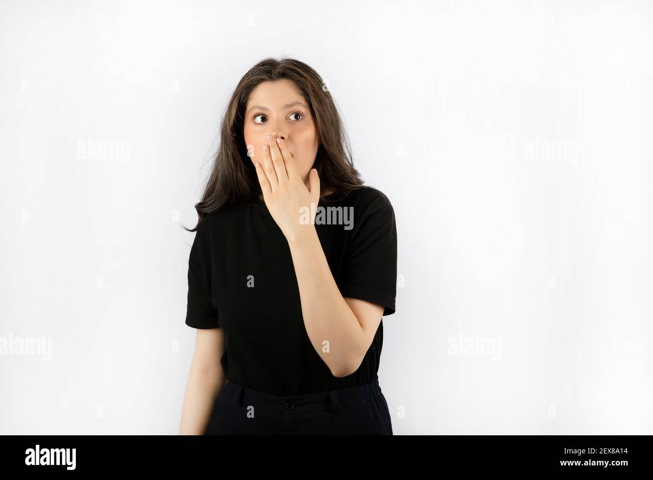 Shocked young woman in black dress holding her hand to her mouth Stock Photo