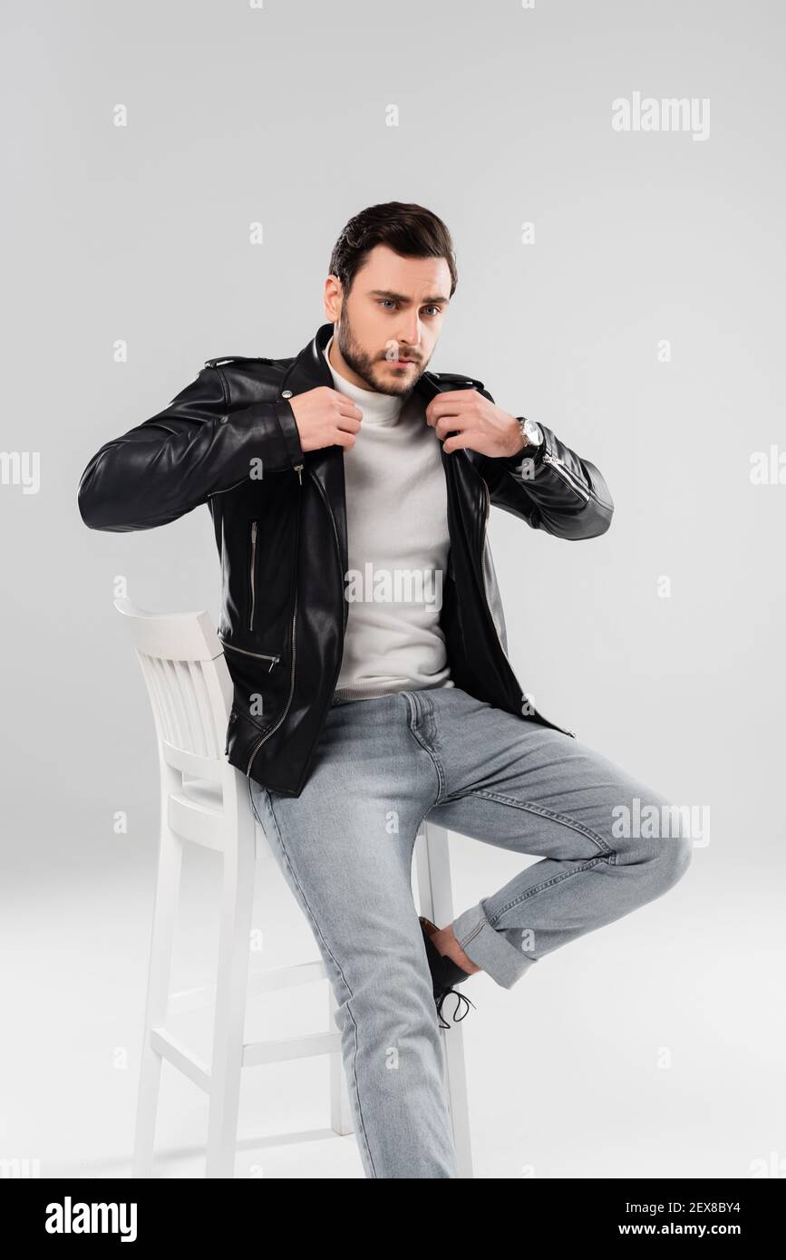 Stylish man wearing leather jacket on chair on grey background Stock Photo  - Alamy