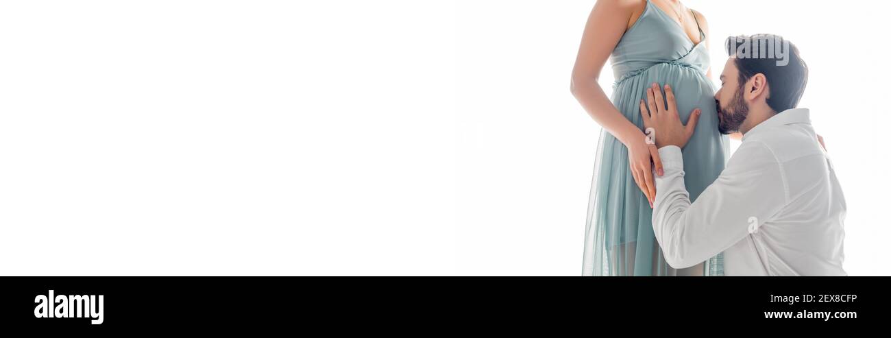 Man kissing belly of pregnant wife in dress isolated on white, banner Stock Photo