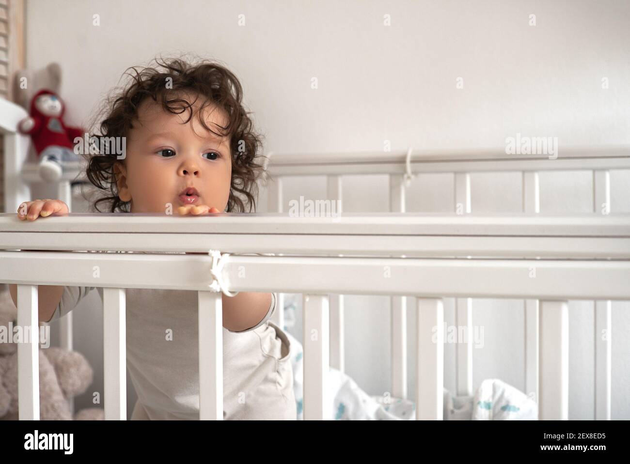 Portrait of a little cute pensive nursing toddler standing in a crib looking at forward. Stock Photo