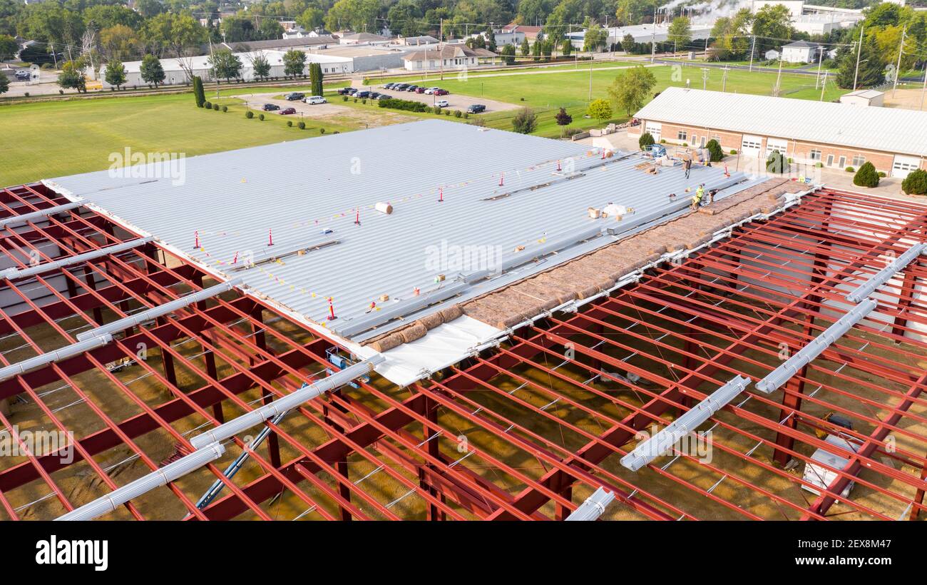 Construction workers installing insulation and roof panels on a large