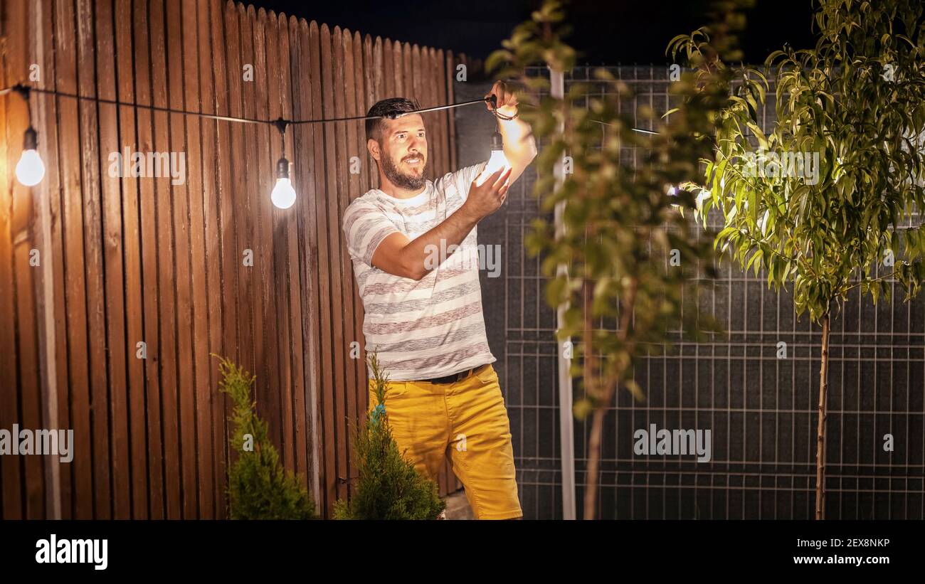 Party time in backyard with happy man hanging string lights in trees Stock Photo