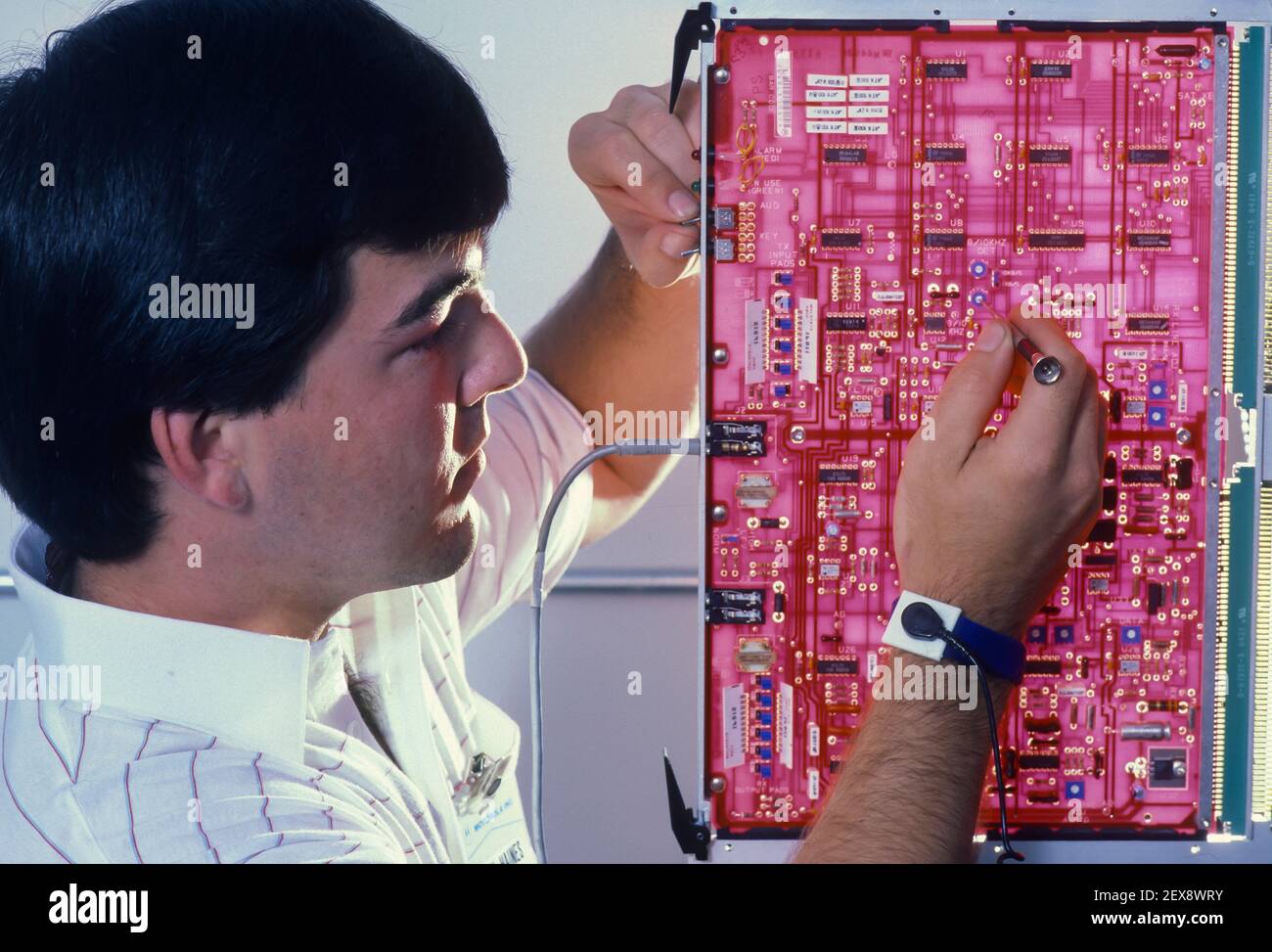SYRACUSE, NEW YORK, USA - Cell phone technician works on circuit board, telecommunications equipment, while wearing static electricity grounding wrist strap. Stock Photo