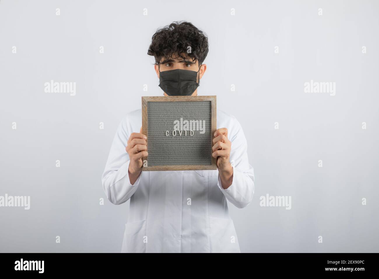 Curly haired young doctor holding board with both hands Stock Photo