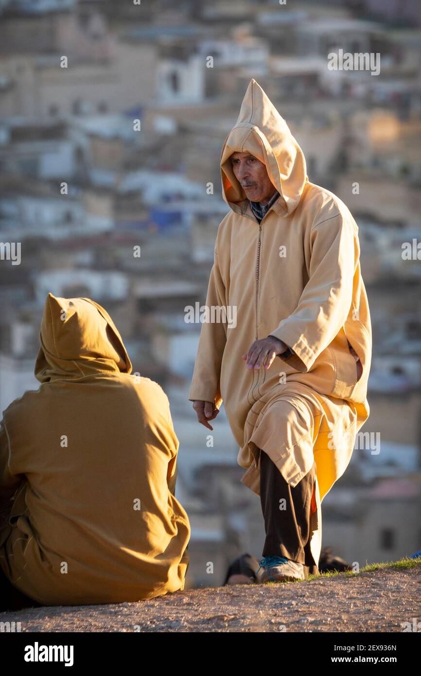 Two local men dressed in traditional clothing interact above the Fes medina, Marinid Tombs, Fes, Morocco Stock Photo
