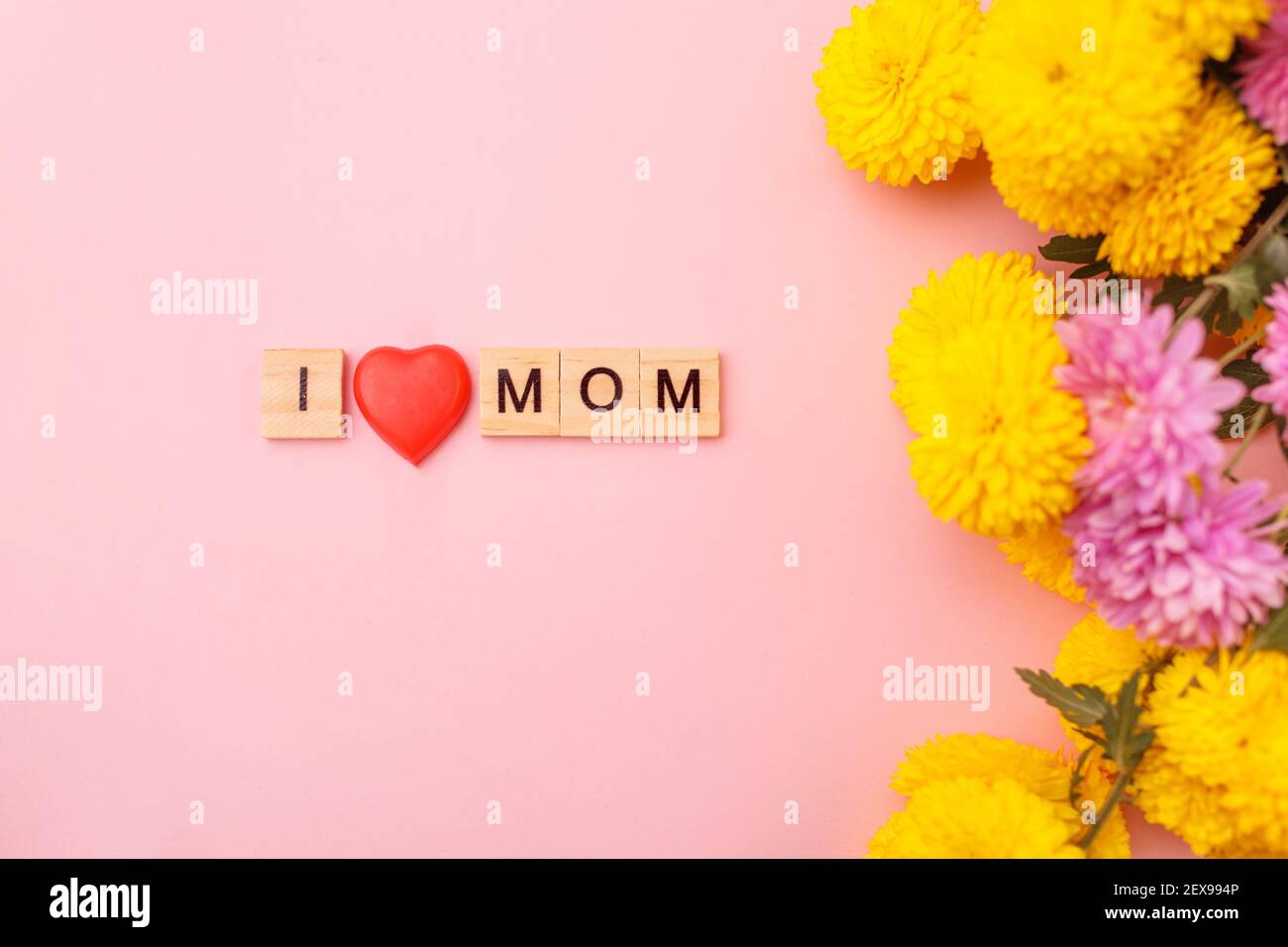 Wooden letters in the phrase I love mom with flowers on a pink background. Greeting card concept for mother day. Stock Photo