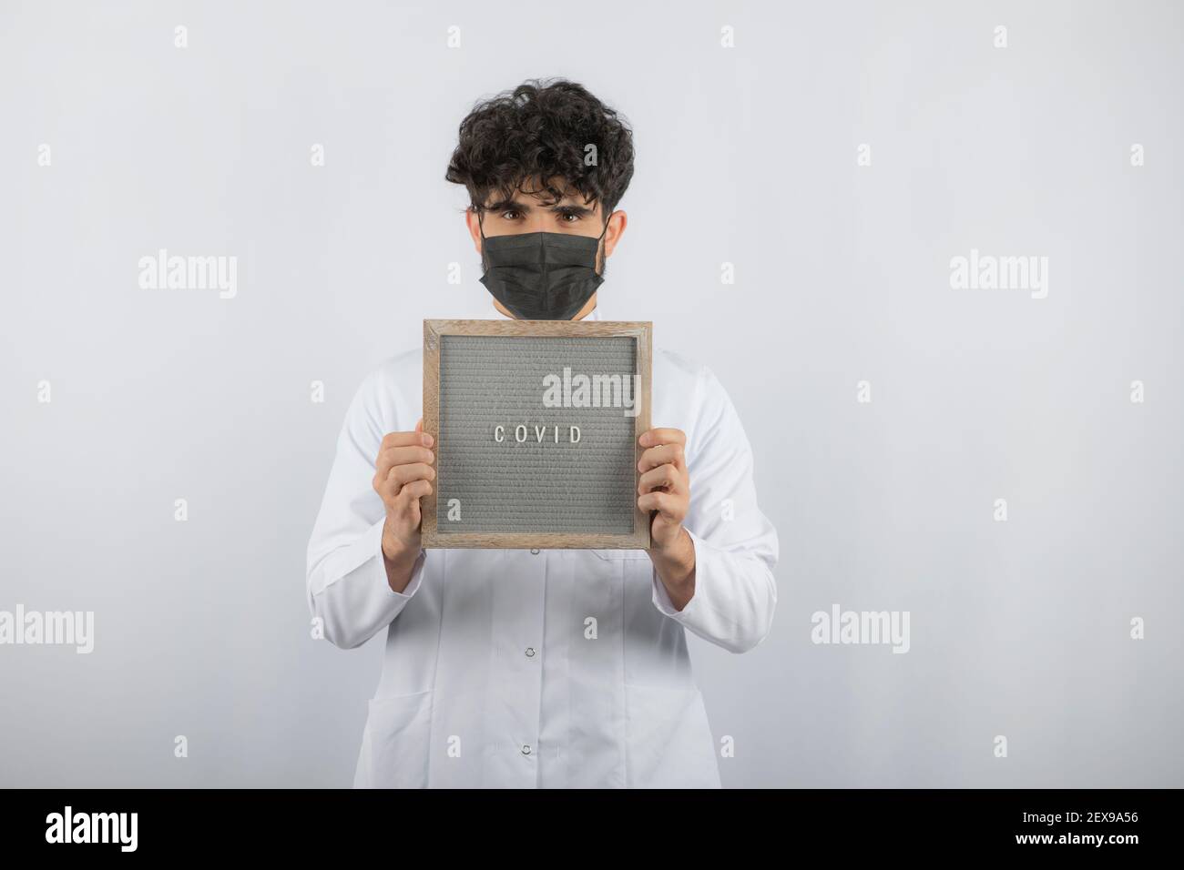 Curly haired young doctor holding board with both hands and directly camera Stock Photo