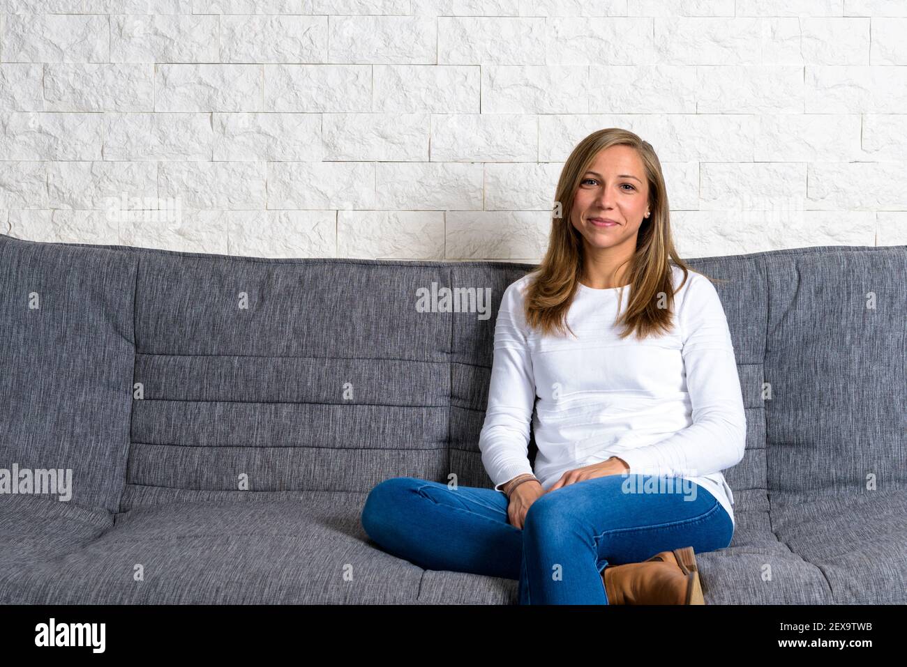 Happy Caucasian woman sitting on the sofa in front of white wall and ...