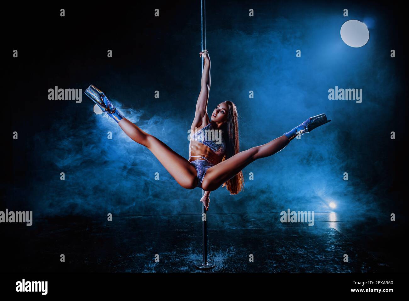 Young sexy woman pole dancing on dark background with smoke and lights Stock Photo