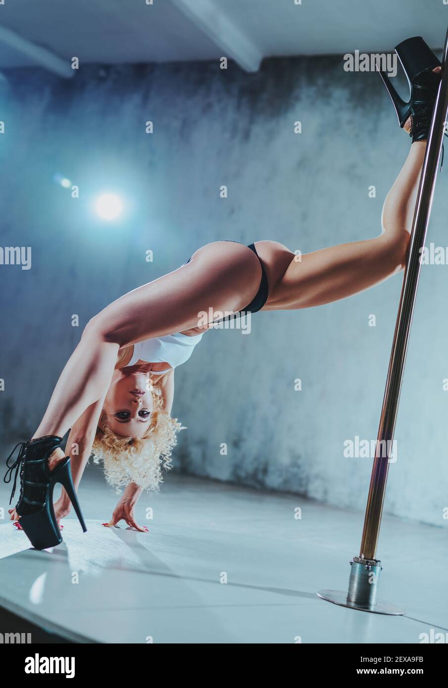 Young slim woman pole dancer in white interior in strange pose stretching legs Stock Photo