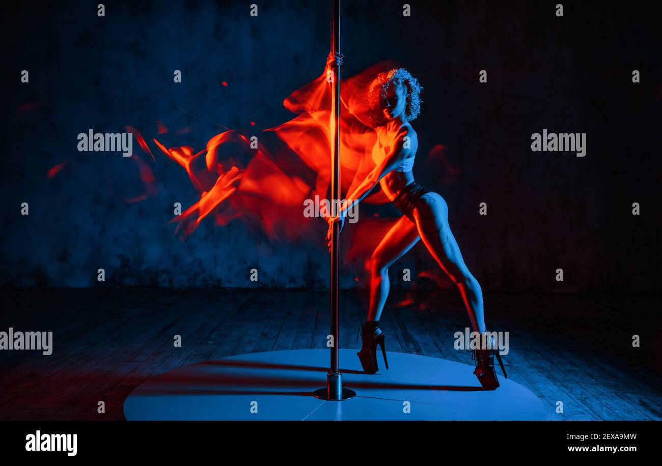 Young woman pole dancer in dark interior. Red fire motion effect. Tattoo on body. Stock Photo