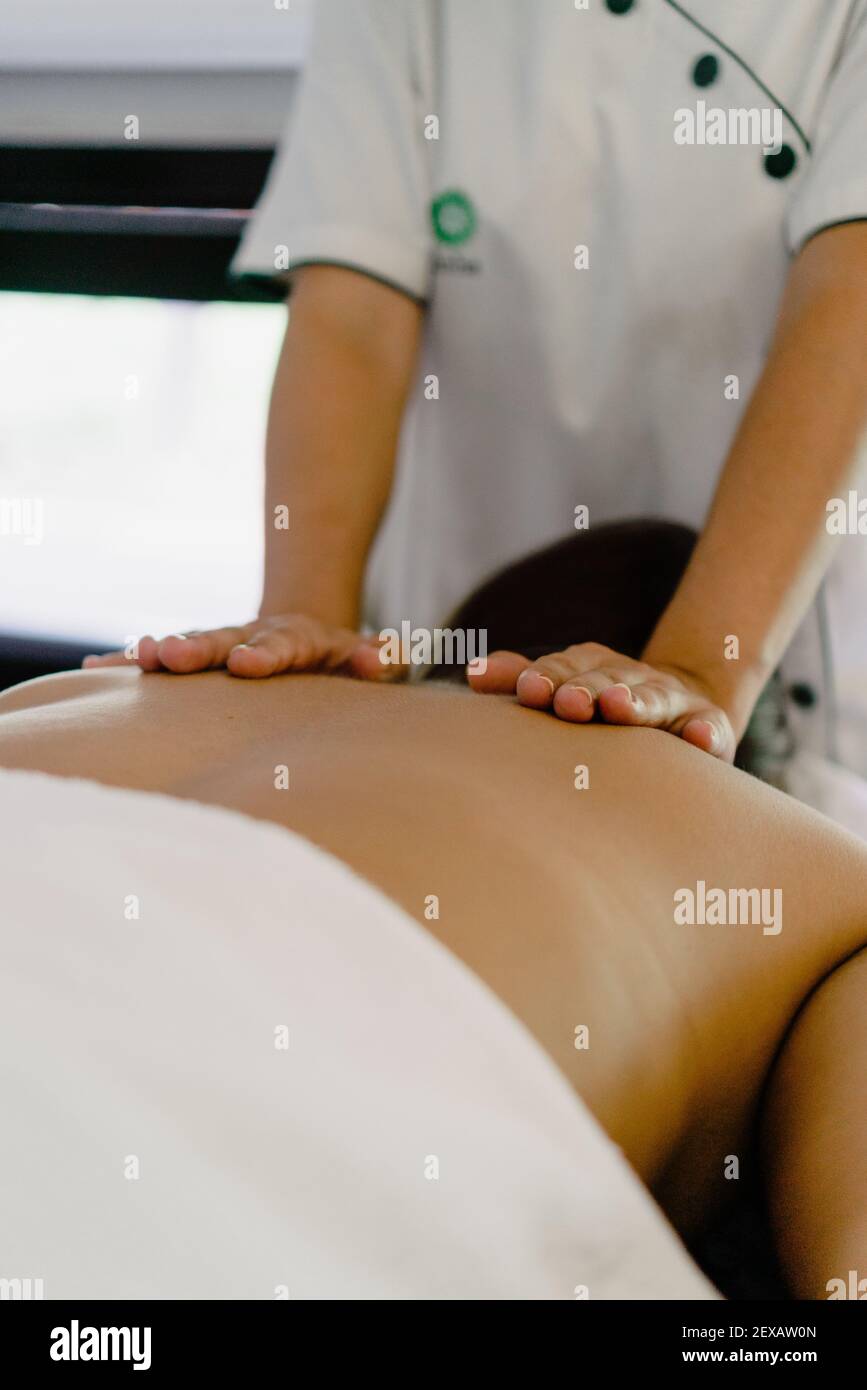 A vertical shot of a masseuse massaging the back of a person lying on a massage table Stock Photo