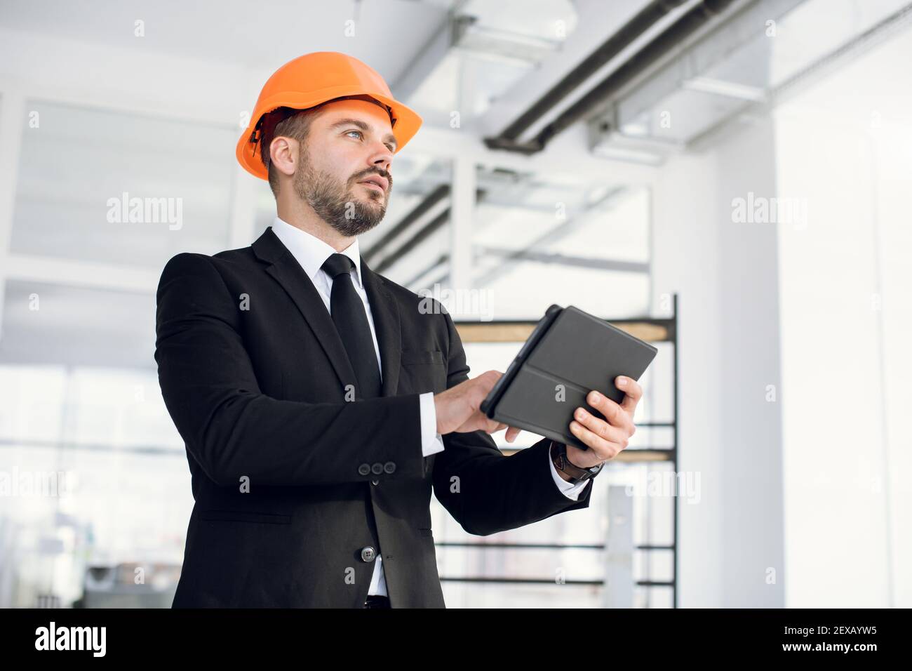 Focused man in suit and hardhat using tablet at work Stock Photo