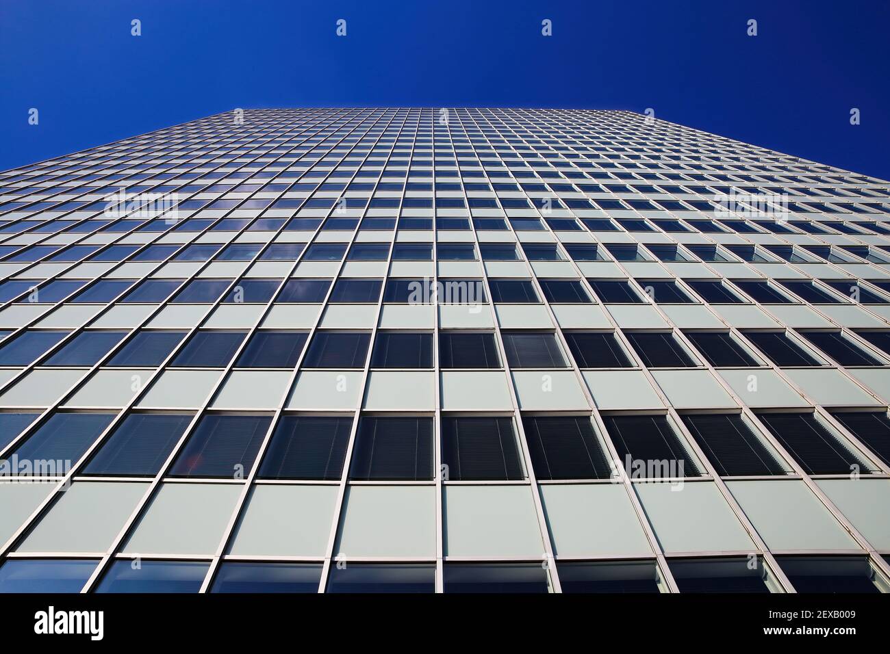 Low angle view on skyscraper facade with geometric symmetrical pattern lines against deep blue cloudless sky Stock Photo