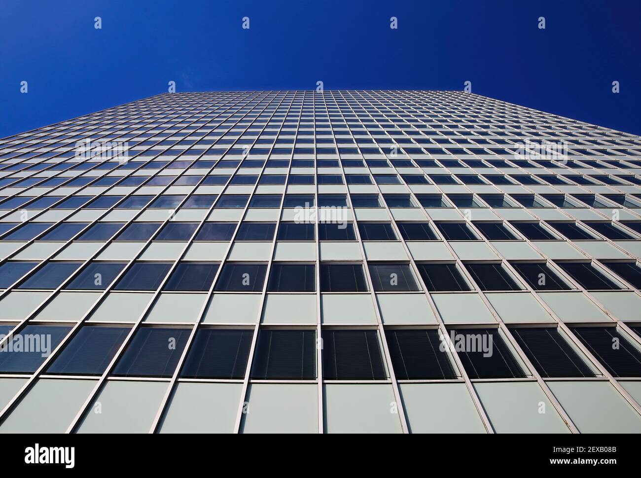 Low angle view on skyscraper facade with geometric symmetrical pattern lines against deep blue cloudless sky Stock Photo