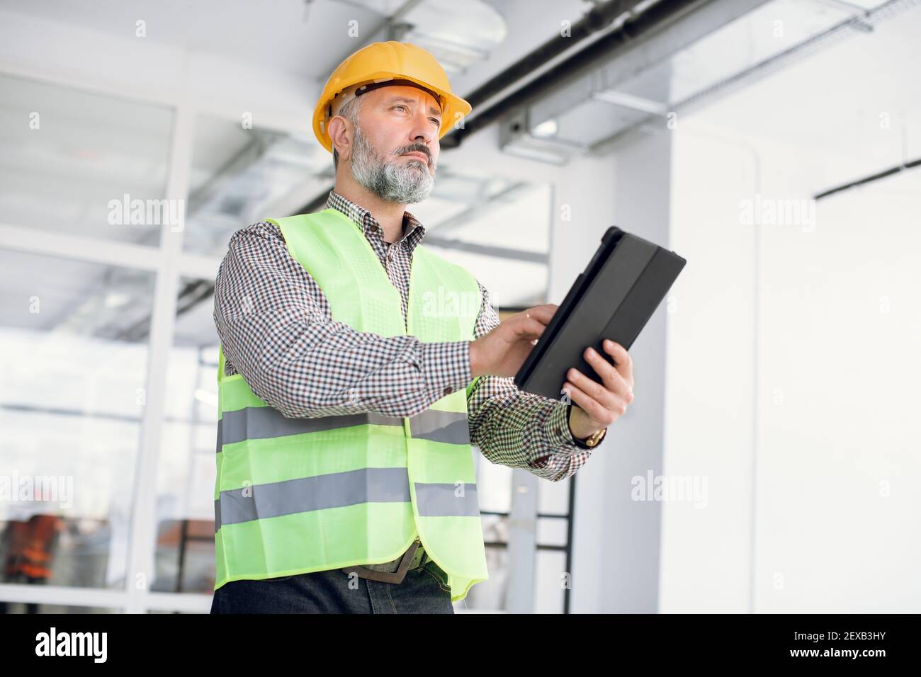 Mature inspector in hardhat working at tablet on object Stock Photo