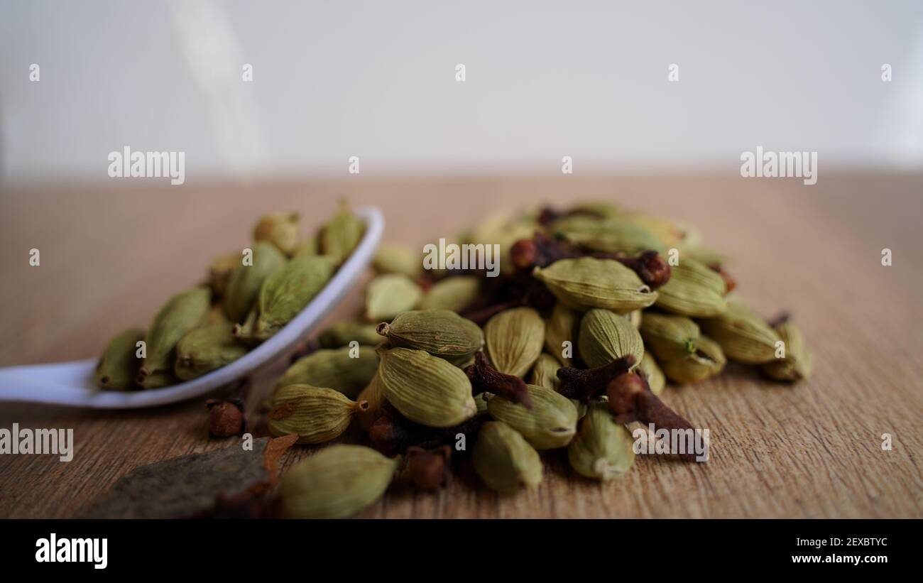 Dry Cardamom pods putting on a wooden background. Fresh elaichi (Elettaria cardamomum) spices heap with white spoon in Kitchen. Indian spice Stock Photo