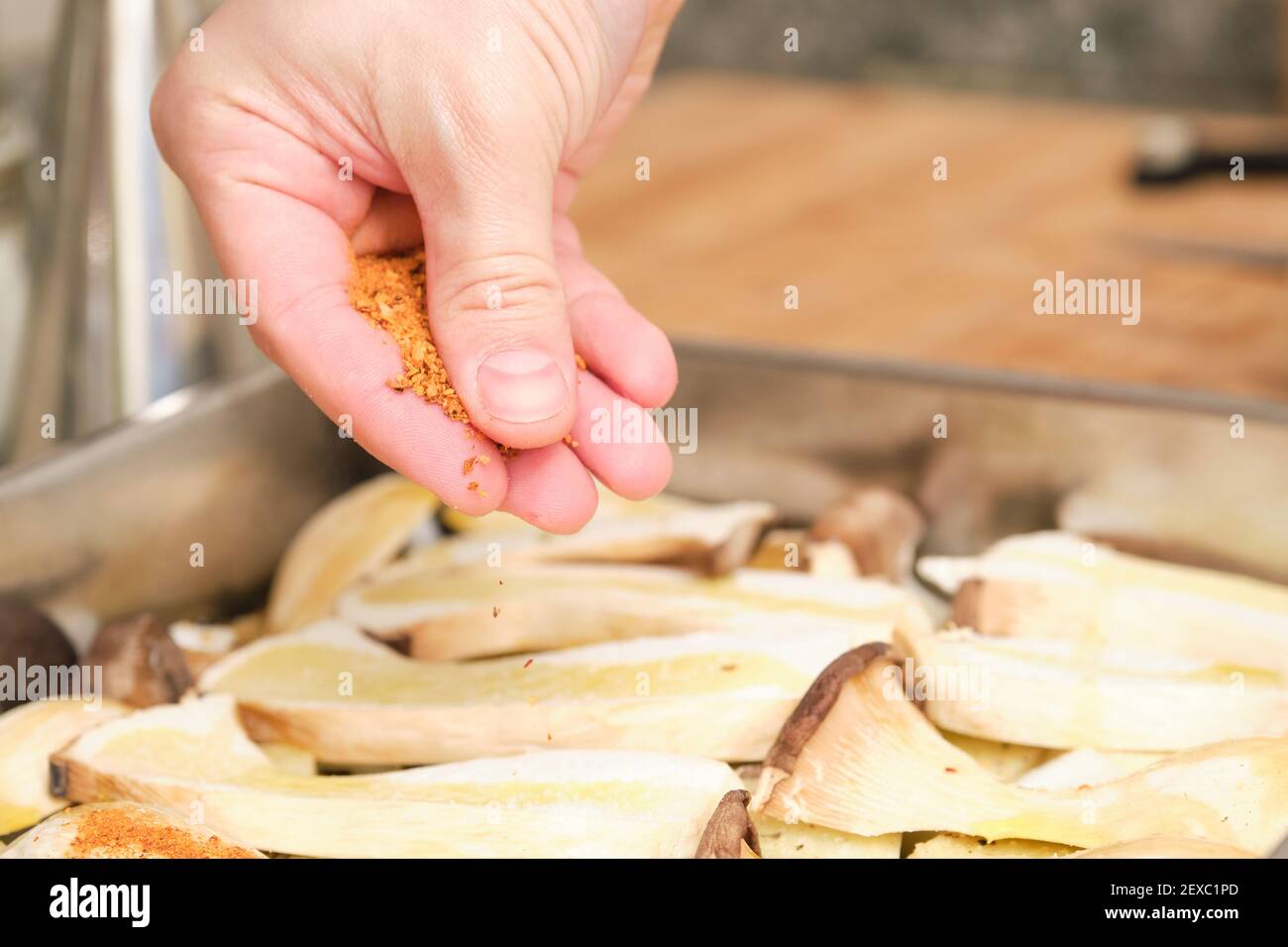 Closeup of man hands adding red spices over sliced king trumpet mushrooms (pleurotus eryngii), potatoes and onions. Cooking process. Mediterranean die Stock Photo