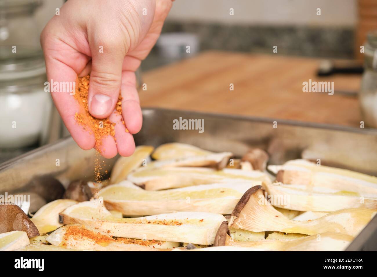 Closeup of man hands adding red spices over sliced king trumpet mushrooms (pleurotus eryngii), potatoes and onions. Cooking process. Mediterranean die Stock Photo