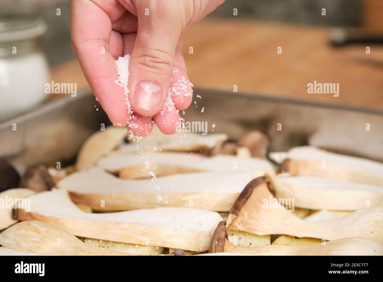 Closeup of man hands adding salt over sliced king trumpet mushrooms (pleurotus eryngii), potatoes and onions. Cooking process. Mediterranean diet. Stock Photo