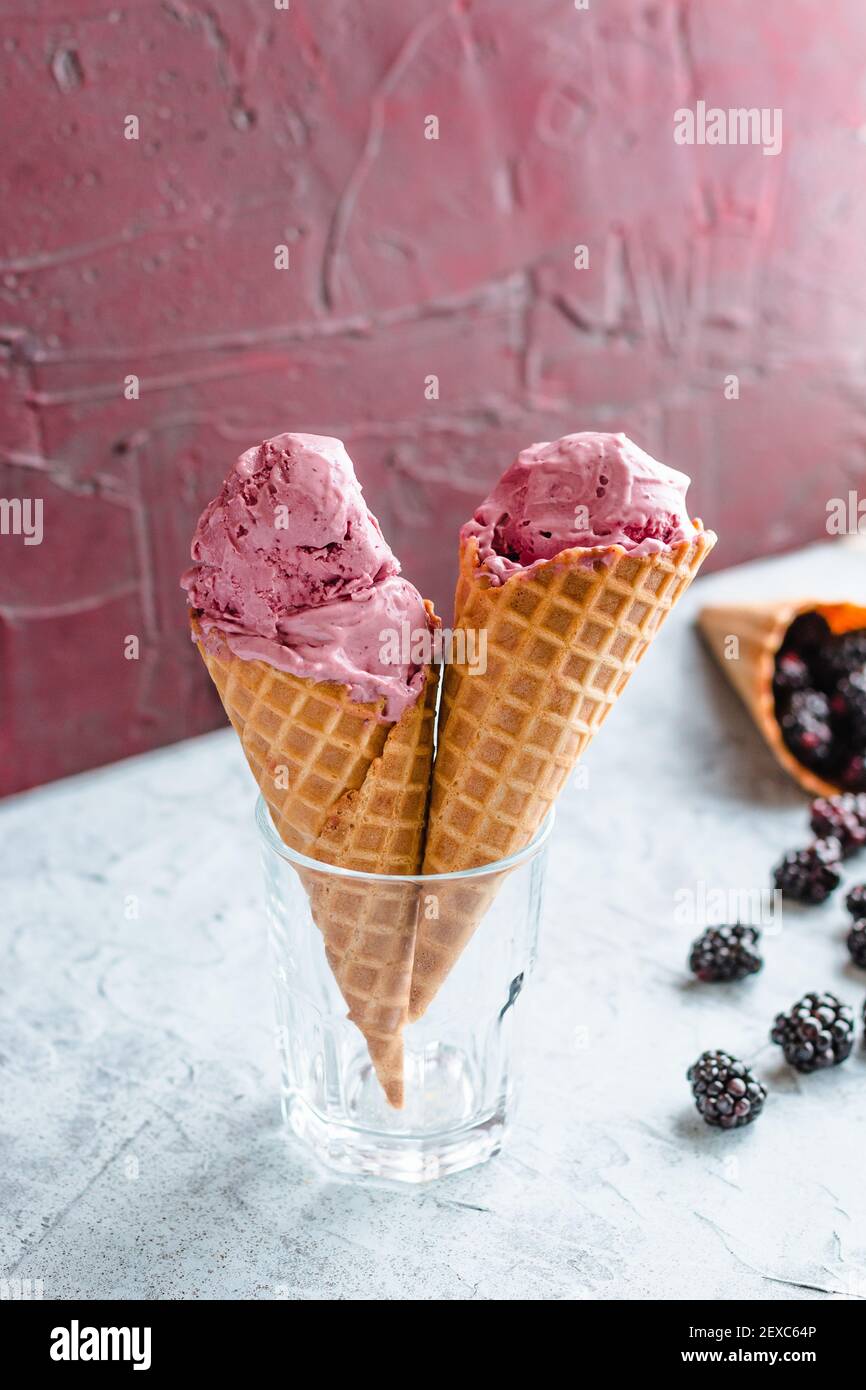 Two blackberry ice cream filled waffle cones are held in a glass, making the shape of a heart. Stock Photo