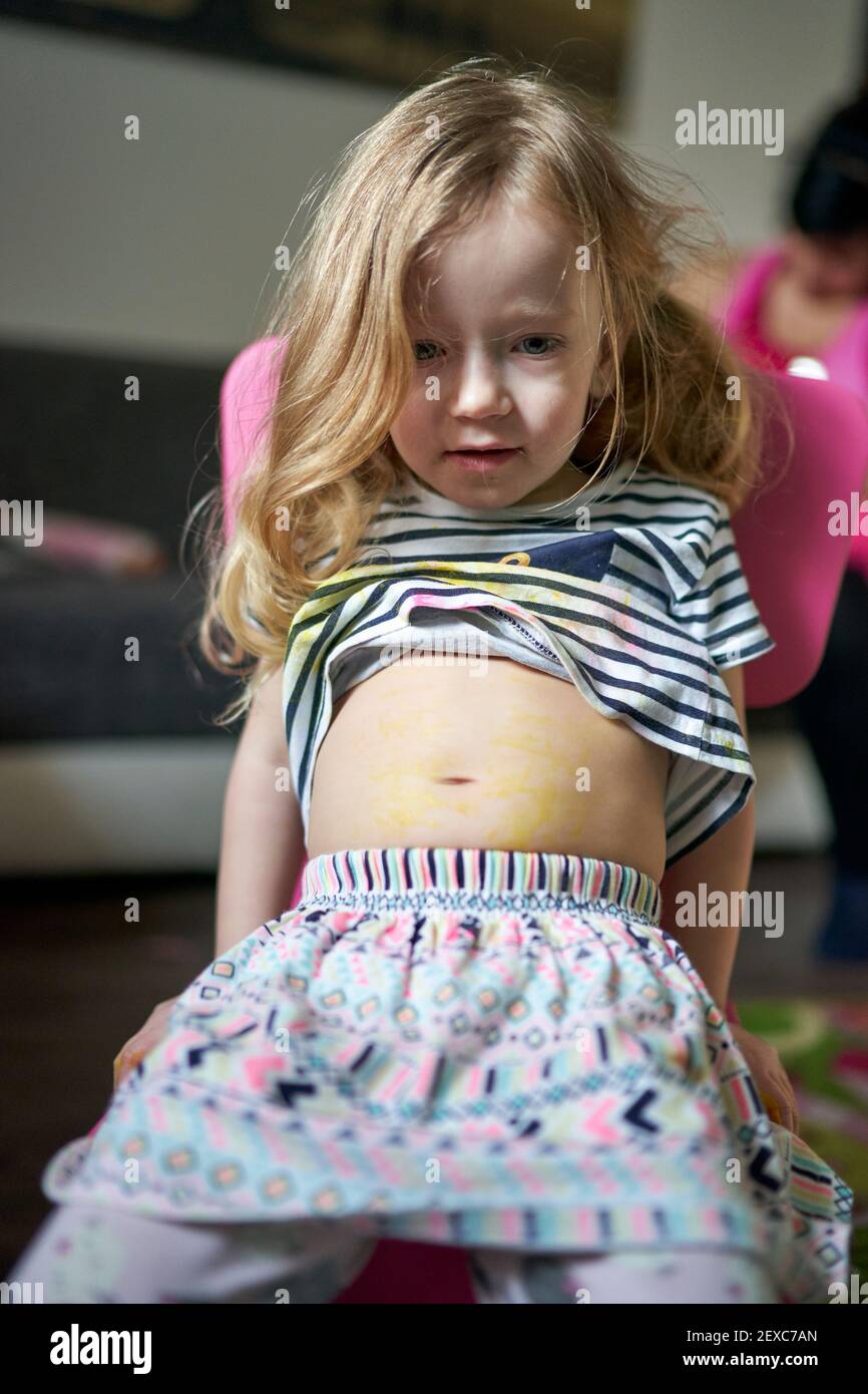 Cute little girl artist sitting on chair showing her pained belly. Stock Photo