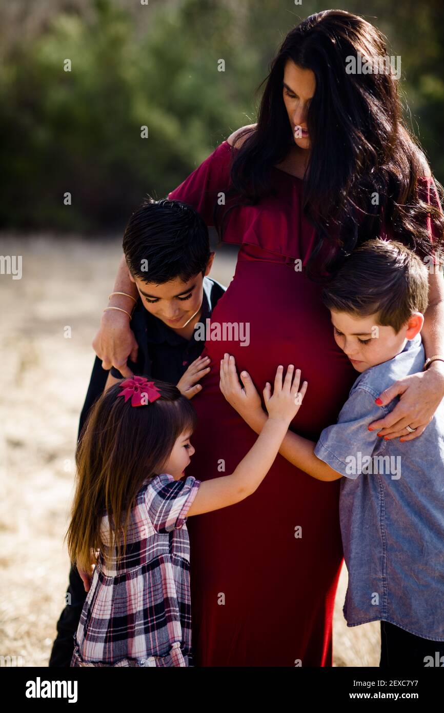 Children Hugging Pregnant Mother in Field in San Diego Stock Photo