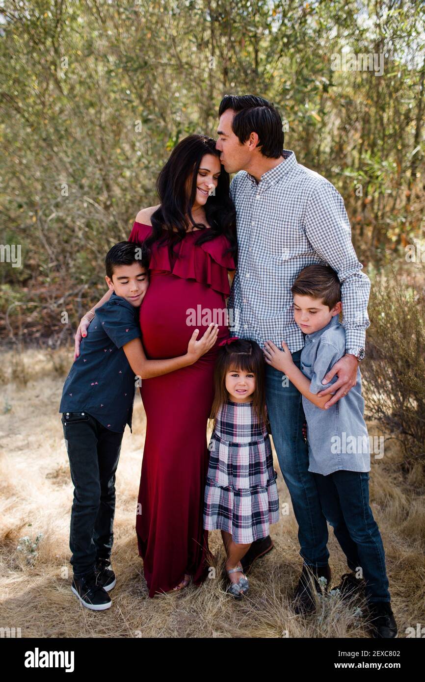 Husband Kissing Expectant Mother with Children in Field in San Diego Stock Photo