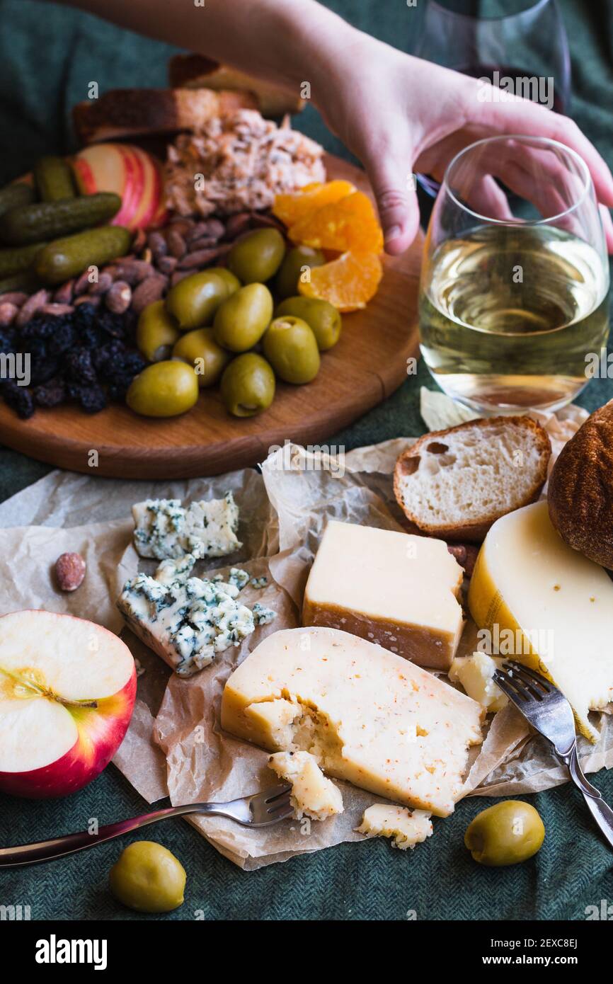 A hand reaching for white wine in a cheese board spread Stock Photo