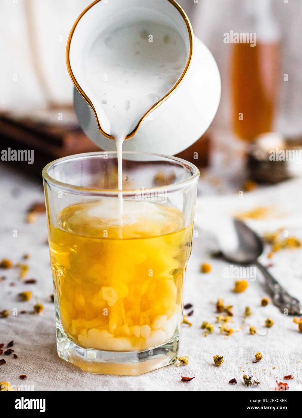 Foamy milk pouring into a glass filled with yellow chamomile tea Stock Photo