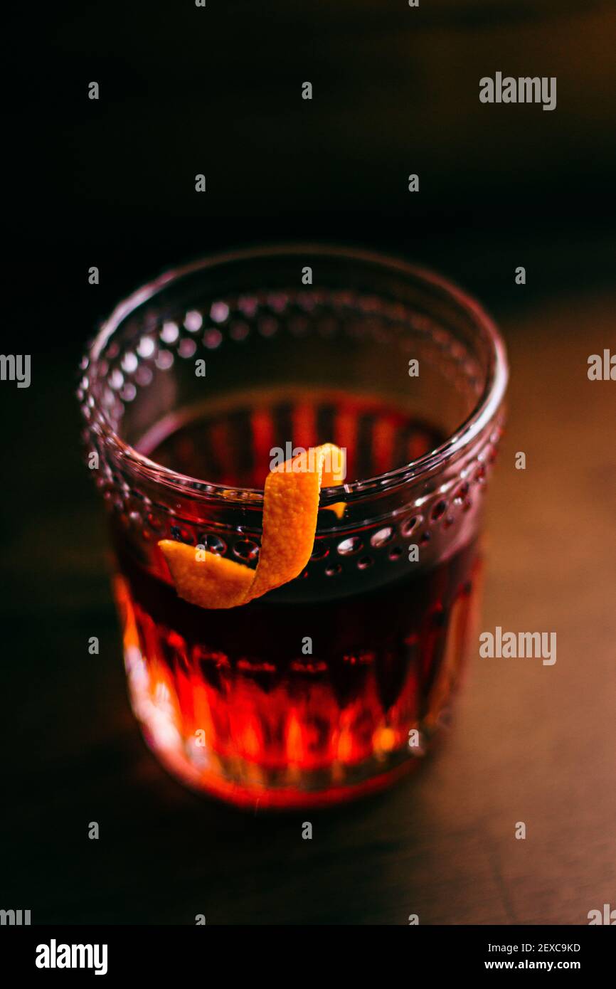 A twist of orange peel hooked onto the edge of a rocks glass holding a Sazerac that is sitting on a wooden surface. Stock Photo