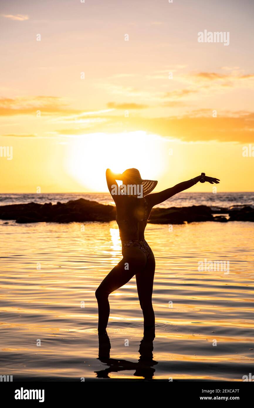 female poses in front of sunset in shallow water wearing hat Stock Photo -  Alamy