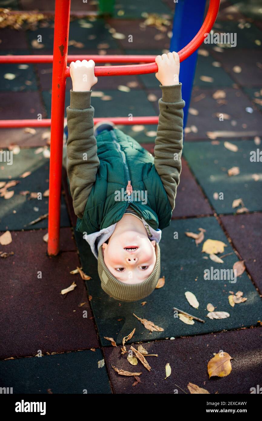 Cute child hanging upside down on monkey bars at autumn playground Stock Photo