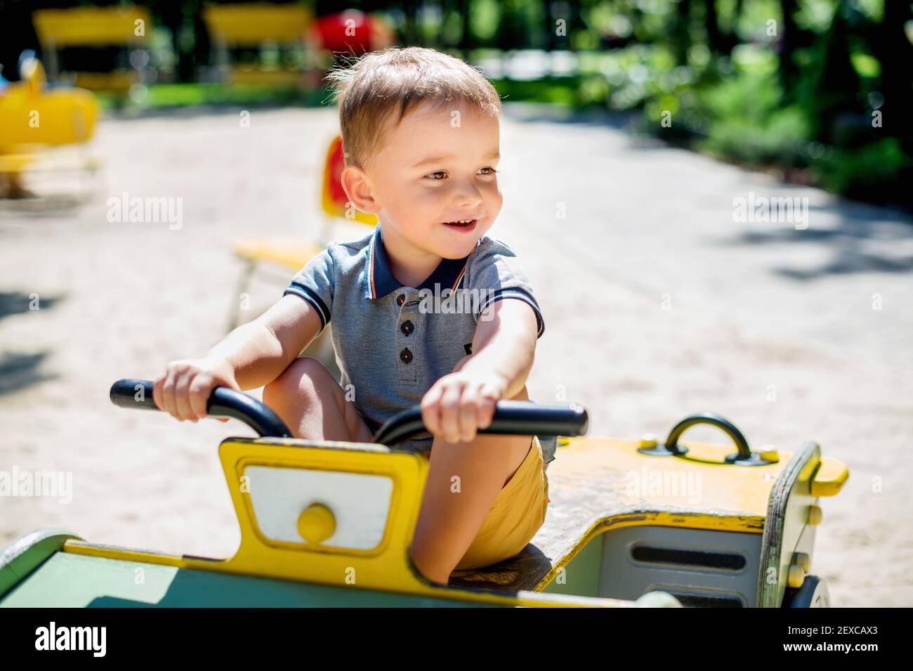 Adorable 2 years old kid riding wooden car at summer park playground Stock Photo