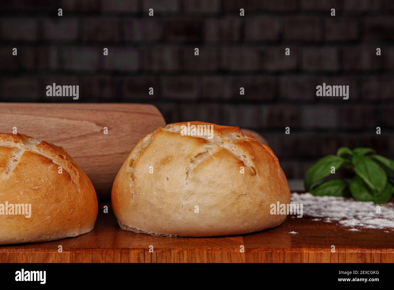 Fresh buns on a wooden board dusted with flour and a rolling pin in the background Stock Photo