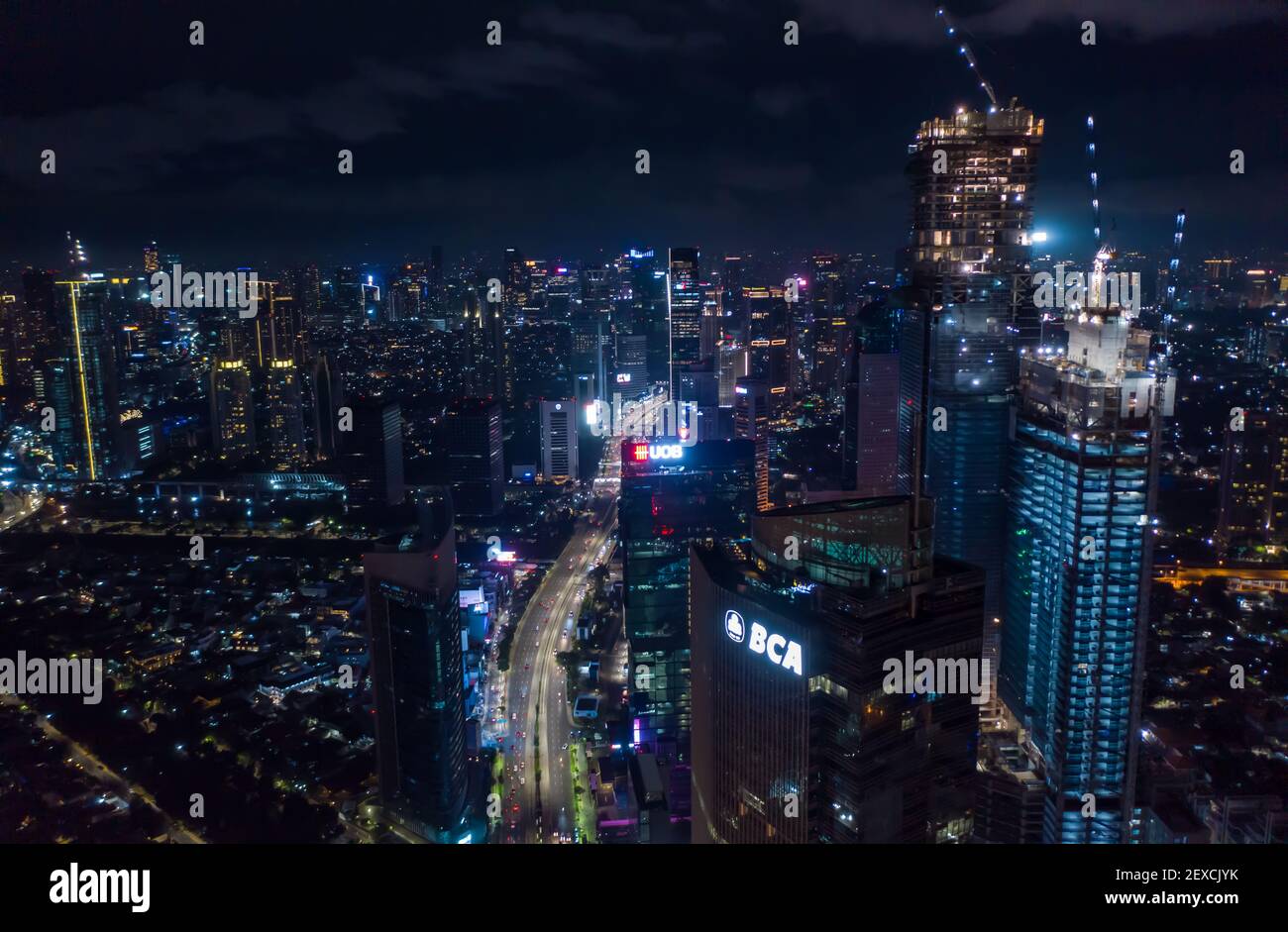 Aerial night view of high rise skyscrapers under construction and modern city center with multi lane highway in Jakarta, Indonesia Stock Photo