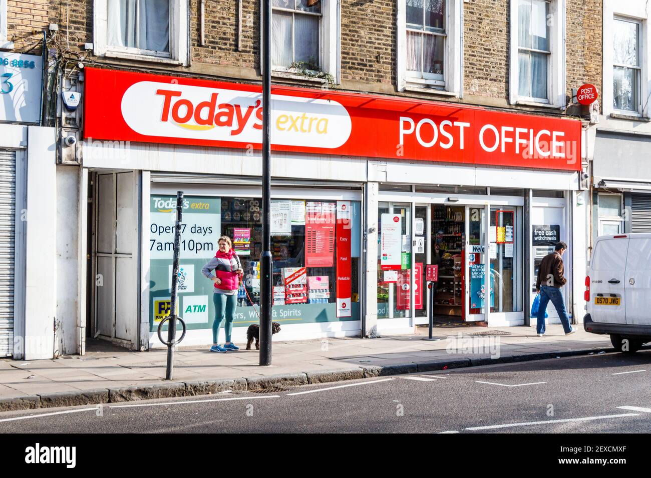 A woman waits outside a local shop and post office, open for essential supplies during the third coronavirus lockdown, Islington, London, UK Stock Photo