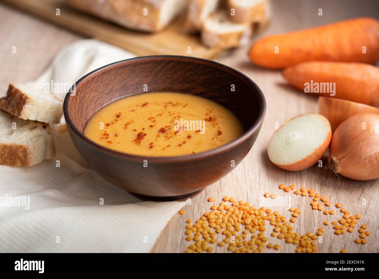 Hot delicious vegetarian red lentil cream soup with ingredients: carrot, onion, and bread on a wooden table, close up. Stock Photo