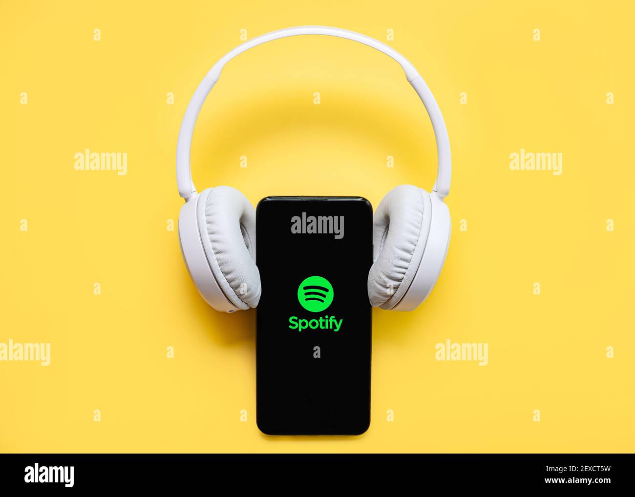 Spotify application icon on black screen of smartphone with white wireless headphone on yellow background Stock Photo