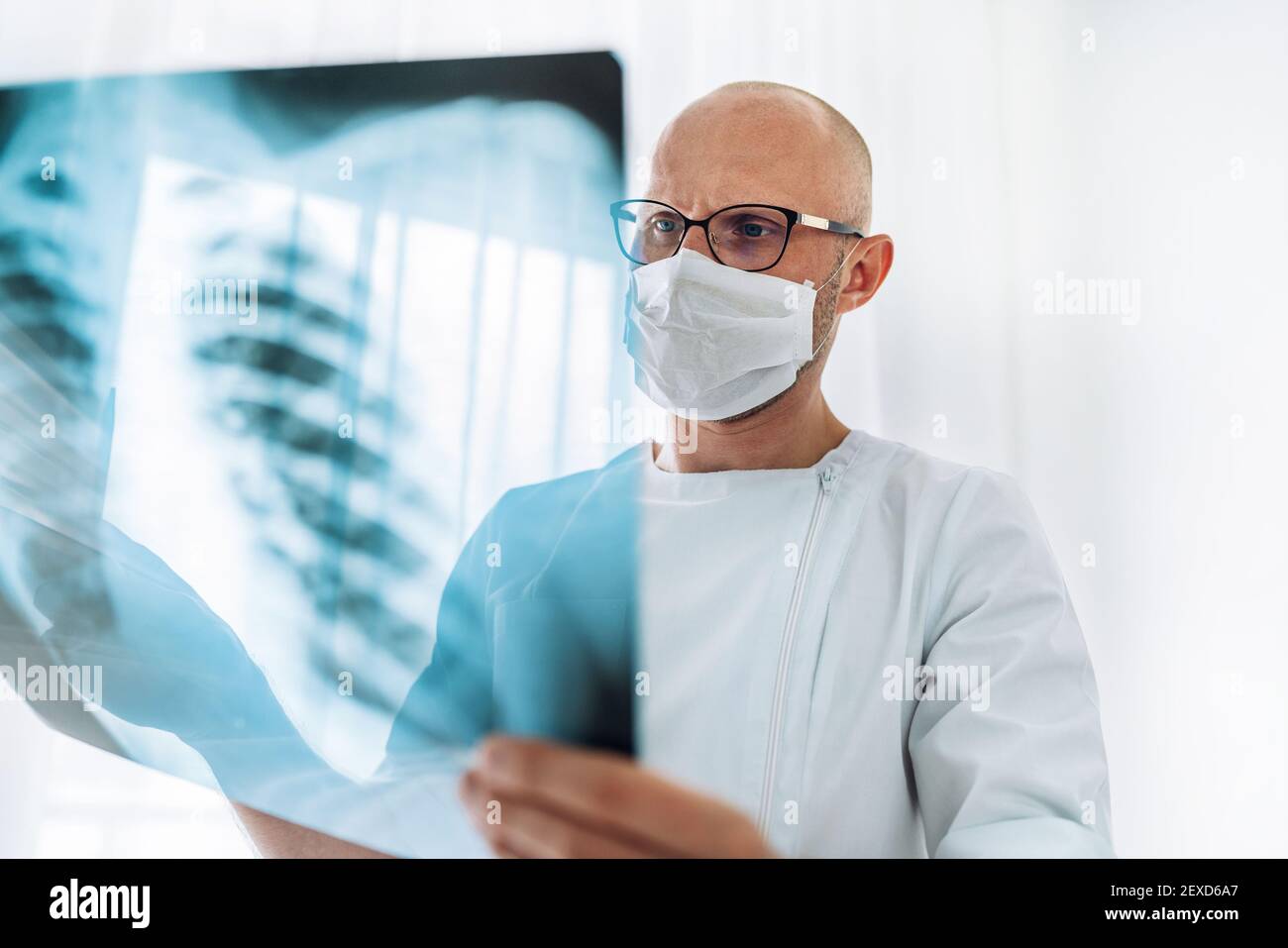 Male doctor in eyeglasses examining the patient chest x-ray film lungs scan at radiology department in hospital.Covid-19 scan body Xray test detection Stock Photo