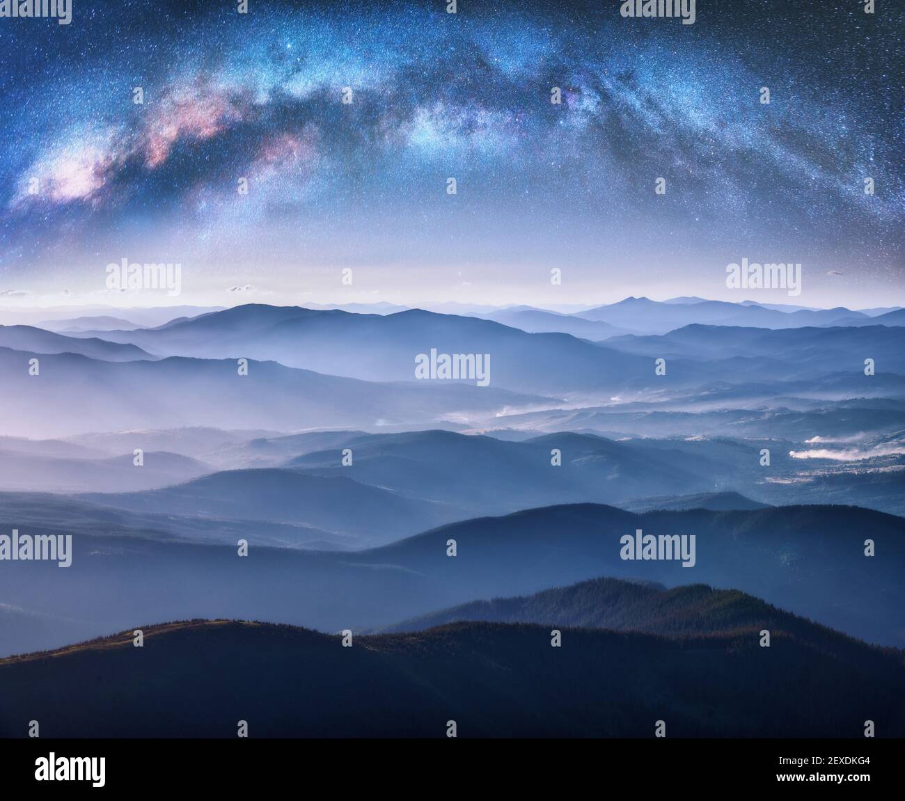 Milky Way arch over the mountains in fog at starry night Stock Photo