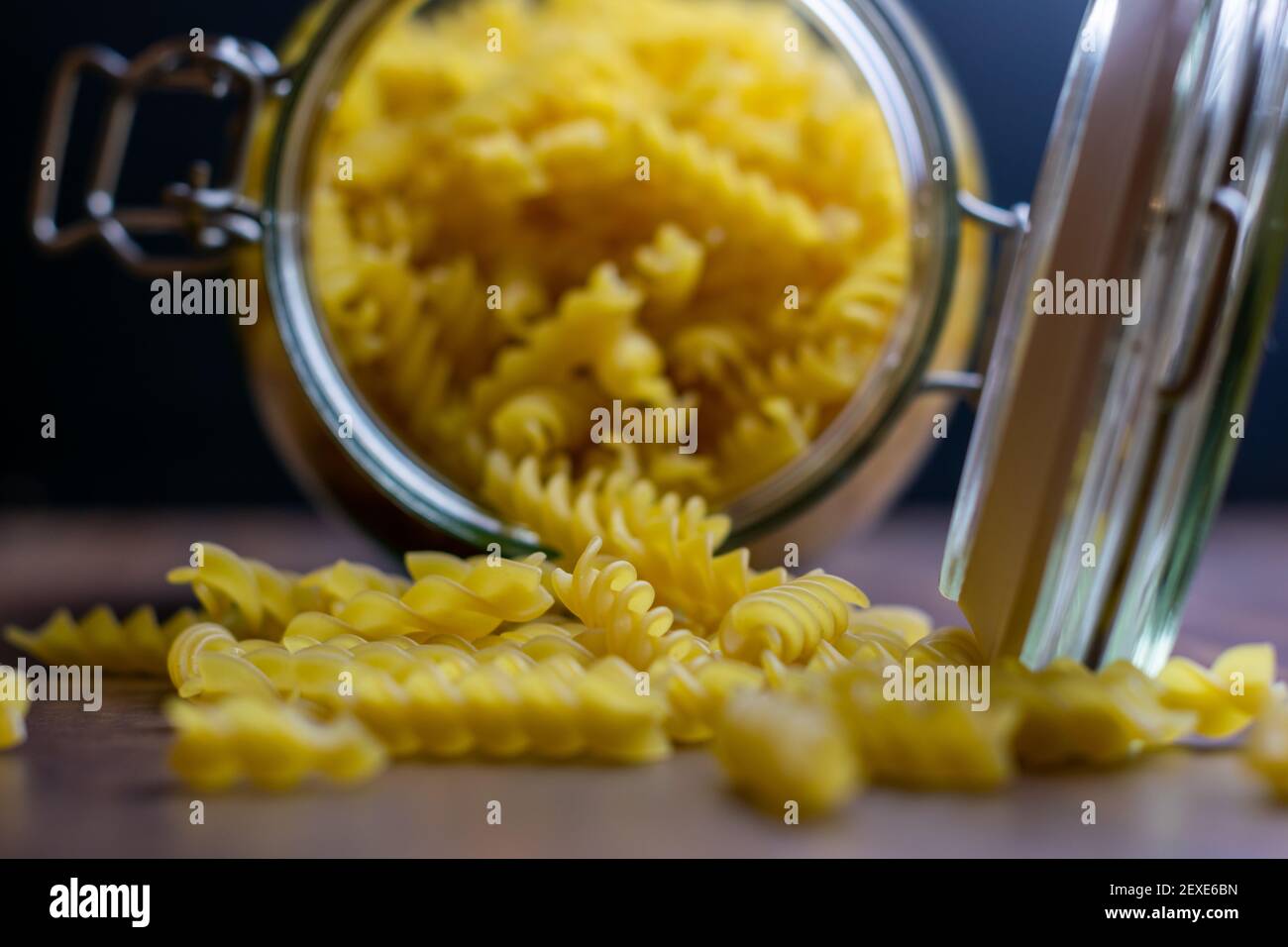 Fussili pasta falling out from a big air tight glass jar. Raw dry pasta in zero waste glass container. Messy food composition on dark background with Stock Photo