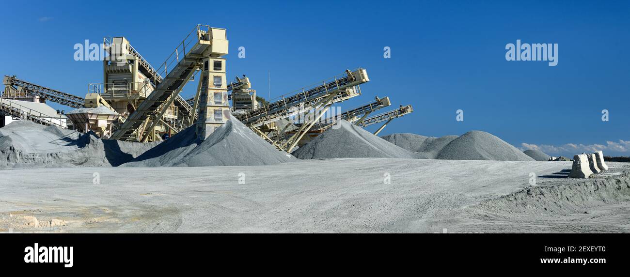 Quarry machines and piles of gravel over blue sky. Stone crushing and screening plant, panoramic view Stock Photo